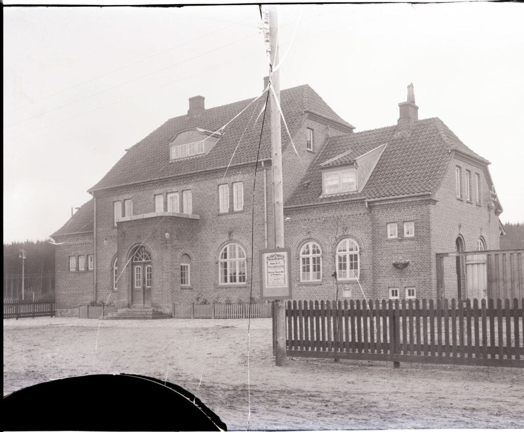 Pladsen foran Hinnerup Station ser meget anderledes ud i dag, end det gjorde dengang det her billede blev taget. Kvaliteten af billedet er ikke fantastisk, og ridserne i det glasnegativ, som billedet er fremkaldt fra er meget tydelige. Foto: Johanne Johannesen/Hinnerup Egnsarkiv.